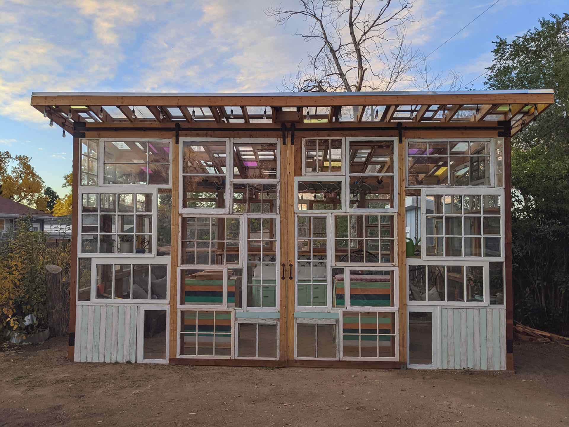 The finished she shed at dusk: a wall of salvaged white window frames under a timber roof with string lights